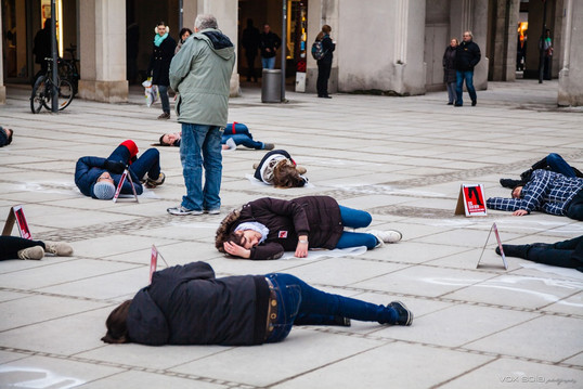 Zeig dein Bein - Stachus - 1. März Aktivistinnen und Aktivisten liegen für einen Flashmob am Münchner Stachus auf dem Boden. Sie liegen auf oder neben aufgesprühten Leichenumrissen mit nur einem Bein. Neben ihnen stehen Warnschilder mit der Aufschrift Danger Mines.