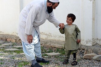 Der sechsjährige Sayed bei einer Therapie. Er lächelt leicht und hält die Hand seines Physiotherapeuten.