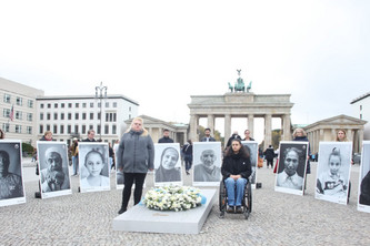 Abgeordnete des Bundestags halten Portraits von Bombenopfern auf dem Pariser Platz. Kranz auf Gedenkstein.